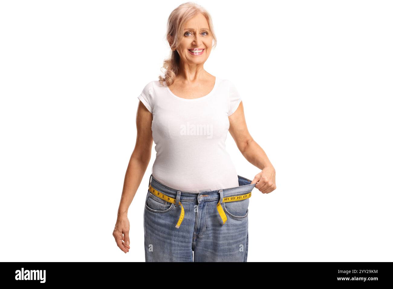 Donna di mezza età che sorride e prova con i jeans, concetto di perdita di peso isolato su sfondo bianco Foto Stock
