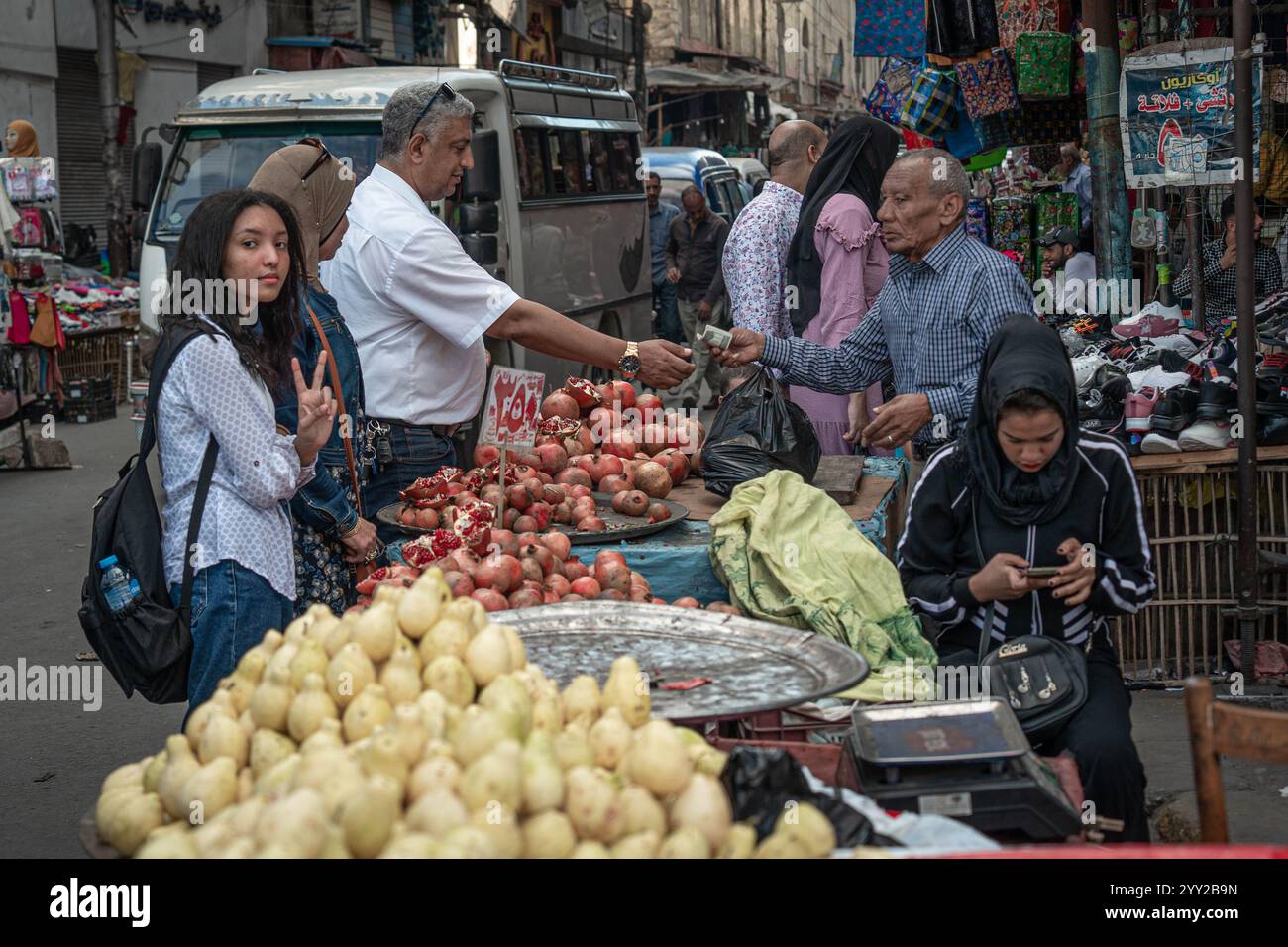 Un vivace mercato di Alexandria con venditori ambulanti che vendono melograni e pere. Un uomo consegna denaro a un venditore mentre gli acquirenti curiosano tra le vivaci bancarelle Foto Stock