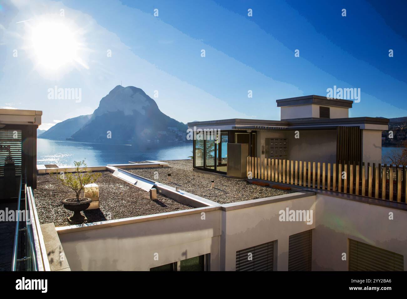 Panorama del lago di Lugano e palazzetto multipiano con piccolo garen (peblles e piante in vaso - fantastica giornata di sole nel cantone ticinese Foto Stock