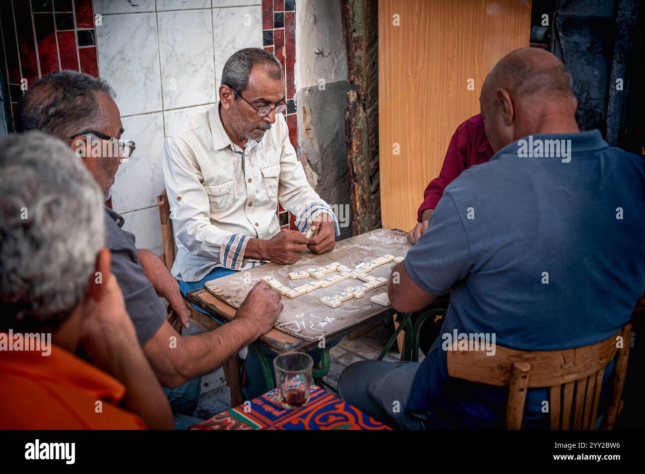 Gruppo di anziani che giocano a domino in un rustico cafй all'aperto ad Alessandria, Egitto. Una scena di strada calda e sociale che cattura la vita quotidiana locale. Foto Stock