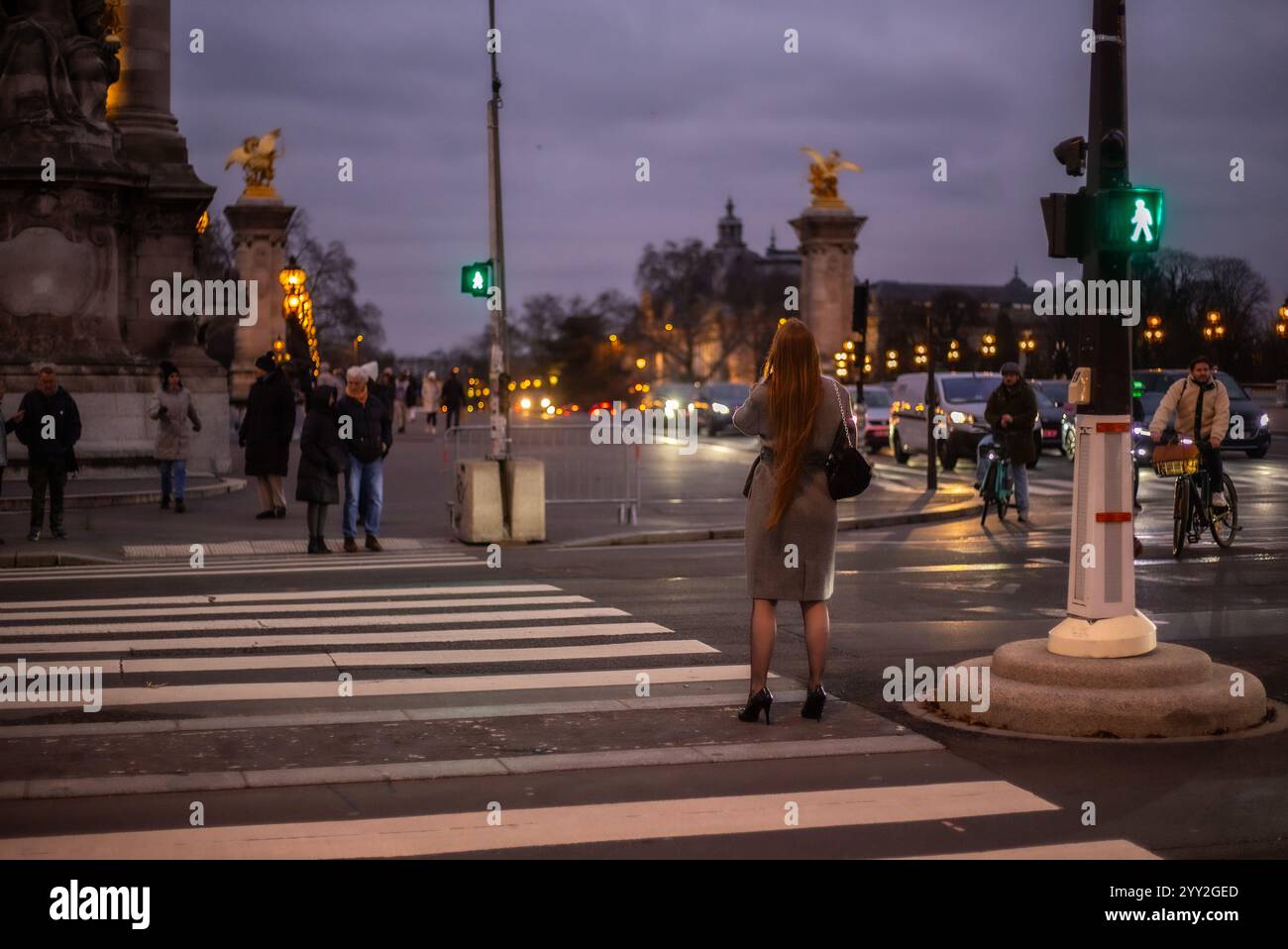 Mentre il crepuscolo oscura il paesaggio, una giovane donna attraente aspetta di attraversare la strada sul ponte di Port Alexandre. Sta indossando un vestito intelligente. Foto Stock
