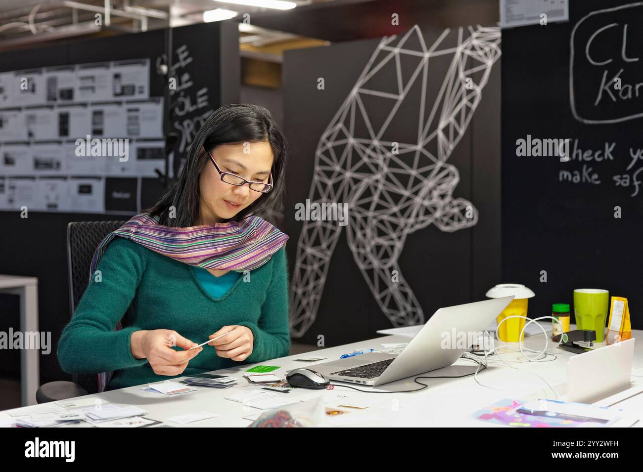 Monaco di Baviera, Germania - 04 febbraio. 2013: Una donna lavora su una scrivania moderna con un portatile e appunti in un ufficio arredato in modo creativo. Gli ambientalisti Foto Stock
