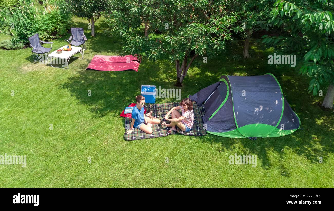 Vista dall'alto del campeggio, madre e figlia si divertono, tenda e attrezzatura da campeggio sotto l'albero, vacanza in famiglia all'aperto Foto Stock