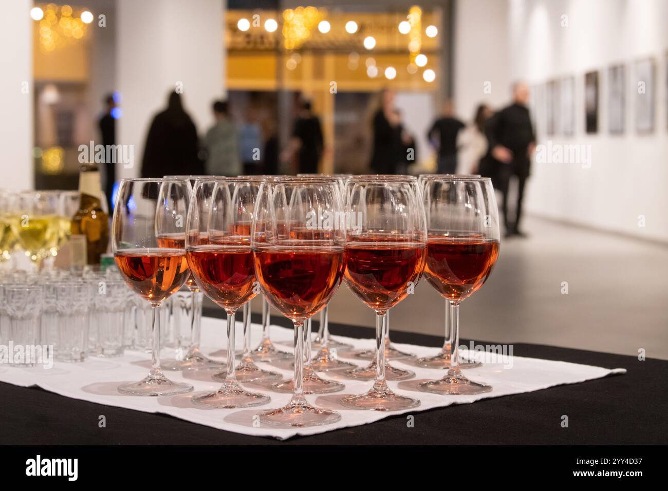Fila di bicchieri pieni di vino sullo sfondo di persone sfocate e dipinti incorniciati alla mostra nella galleria moderna. Foto Stock