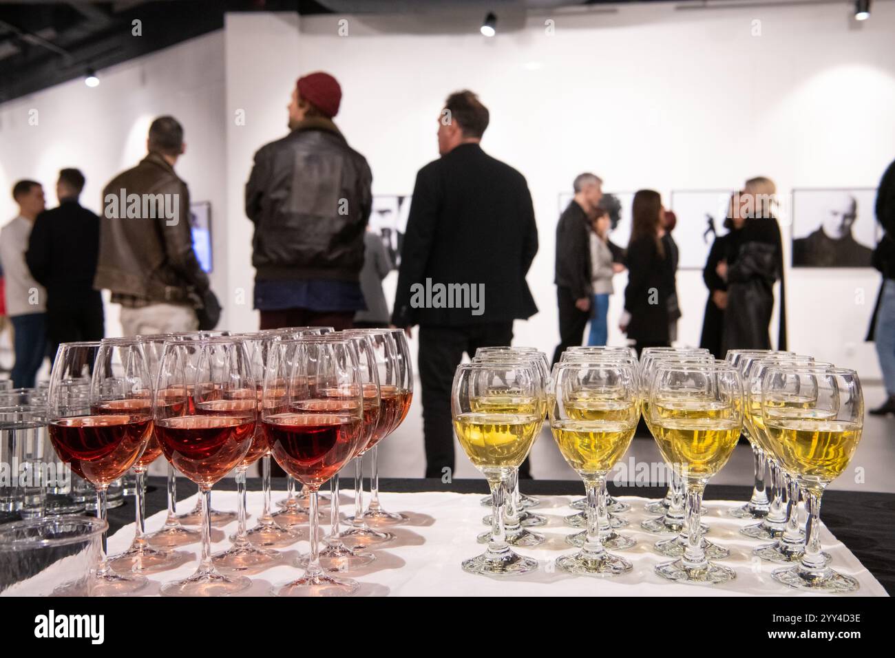 Fila di bicchieri pieni di vino sullo sfondo di persone sfocate e dipinti incorniciati alla mostra nella galleria moderna. Foto Stock