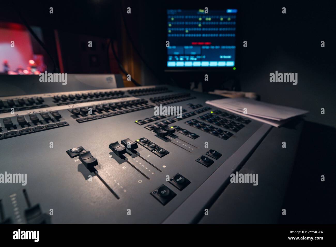 Vista ravvicinata di una console di missaggio audio professionale in un ambiente da studio scarsamente illuminato. Il pannello di controllo è dotato di numerosi pulsanti e cursori per prec Foto Stock