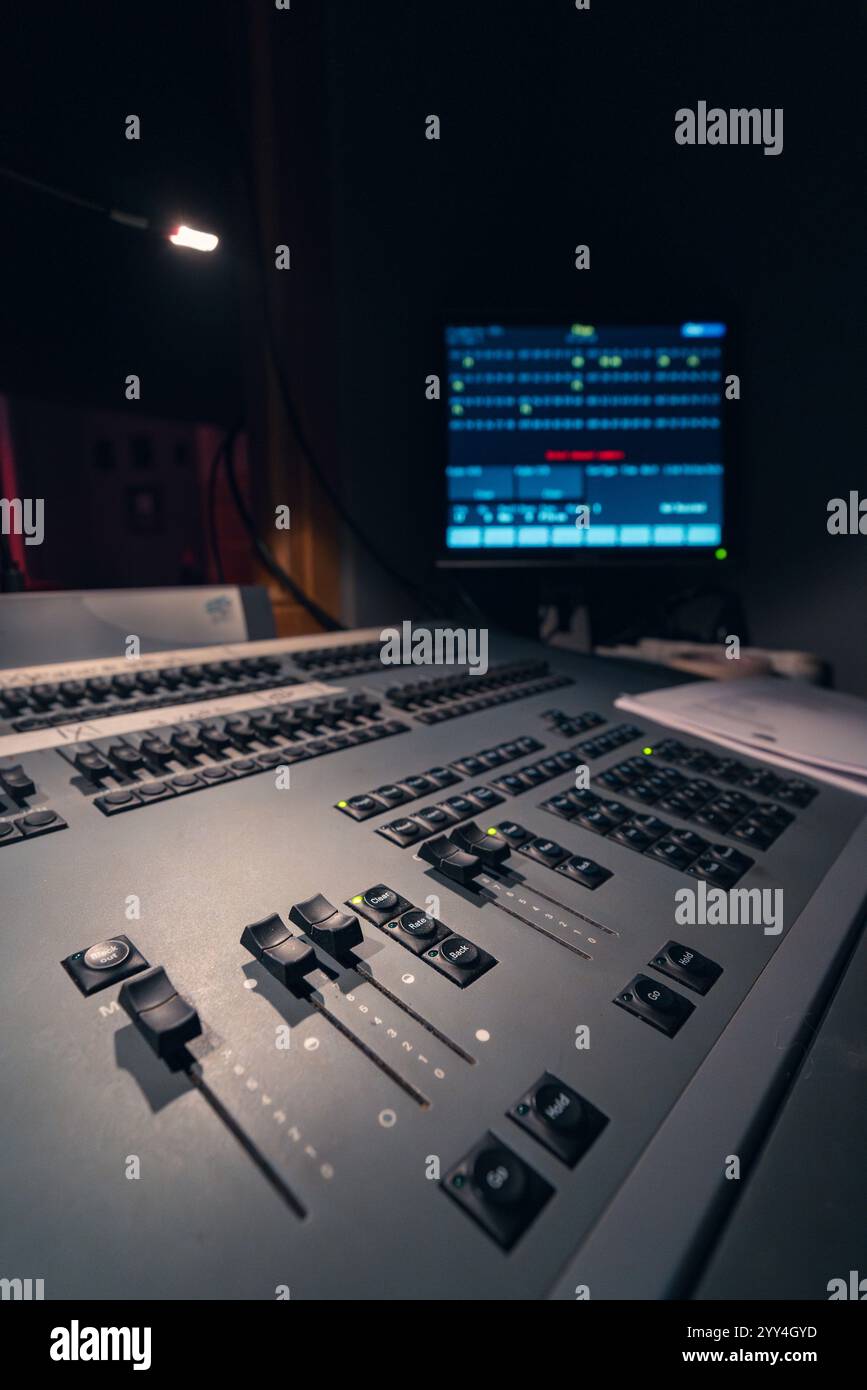 Primo piano di un mixer audio professionale in uno studio poco illuminato. I comandi e i cursori illuminati creano un'atmosfera suggestiva per un audio coinvolgente Foto Stock