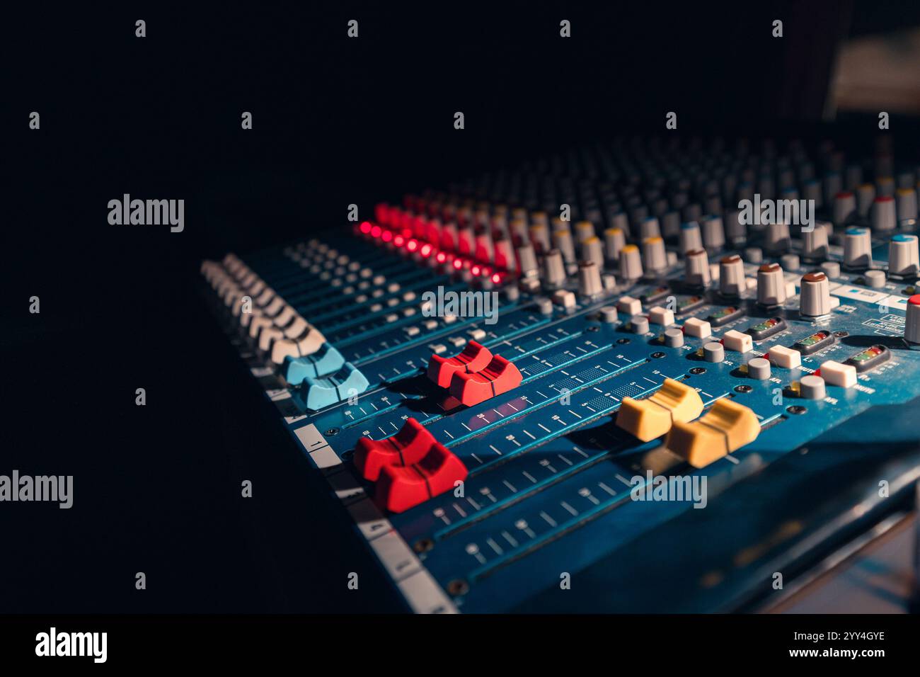Primo piano di una console di missaggio audio professionale con luce soffusa da studio, con cursori e manopole colorati per il controllo audio e la produzione musicale. IO Foto Stock
