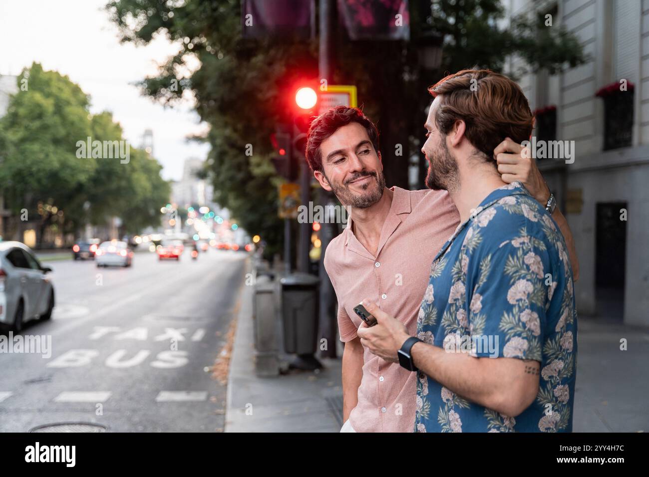 Una coppia gay amorevole condivide uno sguardo affettuoso su una vivace strada cittadina al crepuscolo, creando un momento di intimità in mezzo alla vita urbana Foto Stock