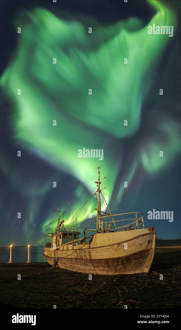 Un'incredibile esibizione dell'aurora boreale danzerà su una barca abbandonata sulla costa islandese, creando una scena notturna surreale e ipnotica ricca di spirito Foto Stock