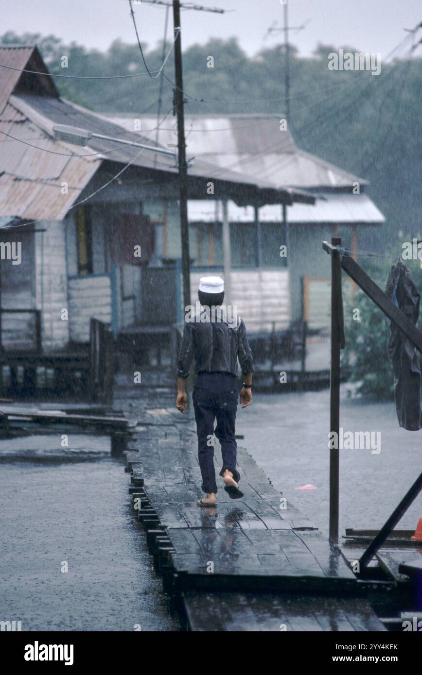 Singapore, allagata, uomo che cammina a casa attraverso la piattaforma di legno fino alla sua casa kampong a Sembawang. Settembre 1983. Un kampong è un tipo di insediamento nei paesi del sud-est asiatico. Queste abitazioni sono generalmente piuttosto basilari e potrebbero mancare di elettricità, acqua e gas. HOMER SYKES anni '1980 Foto Stock