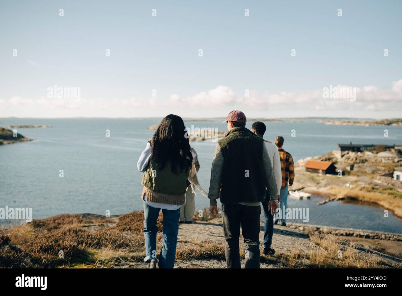 Vista posteriore di una giovane donna che cammina con un amico maschio verso il mare durante il giorno di sole Foto Stock