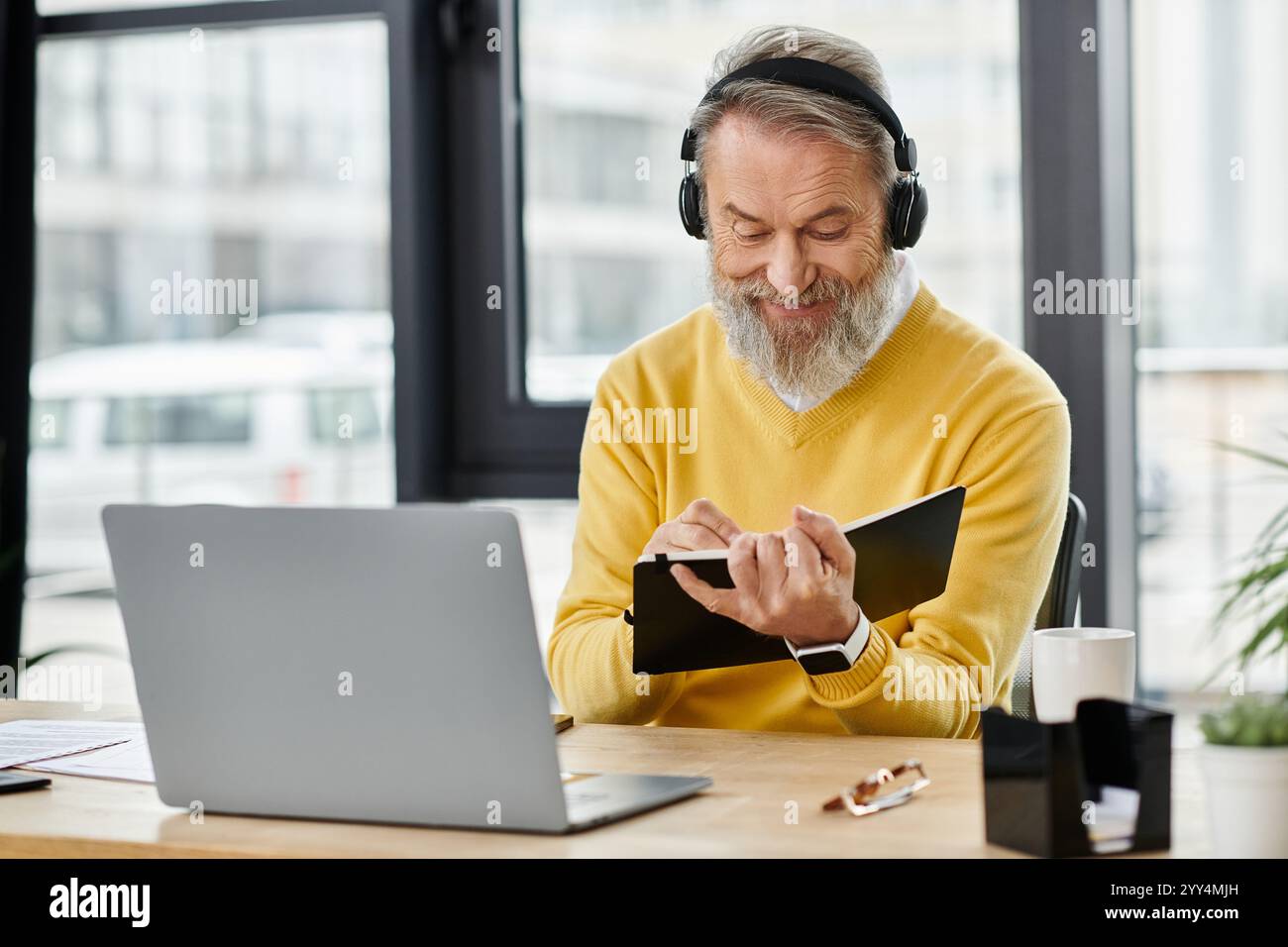 Bell'uomo maturo con le cuffie scrive appunti mentre si siede a una scrivania in un bar moderno. Foto Stock