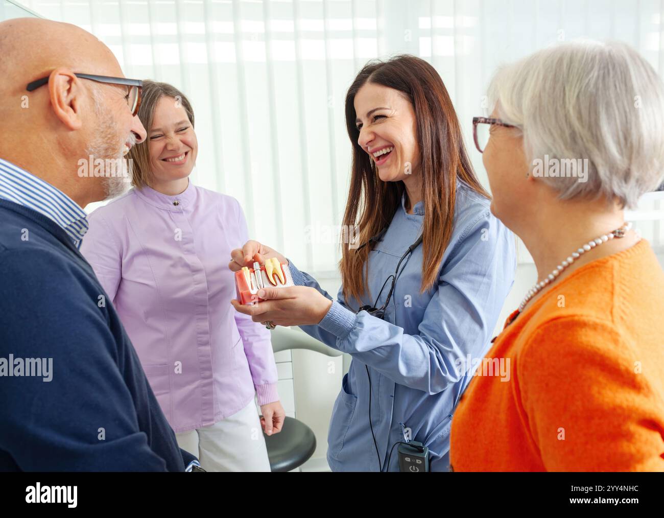 Dentista che mostra il modello dentistico al paziente anziano, che spiega la procedura di impianto dentale in clinica, assistenza sanitaria e concetto di medicina Foto Stock