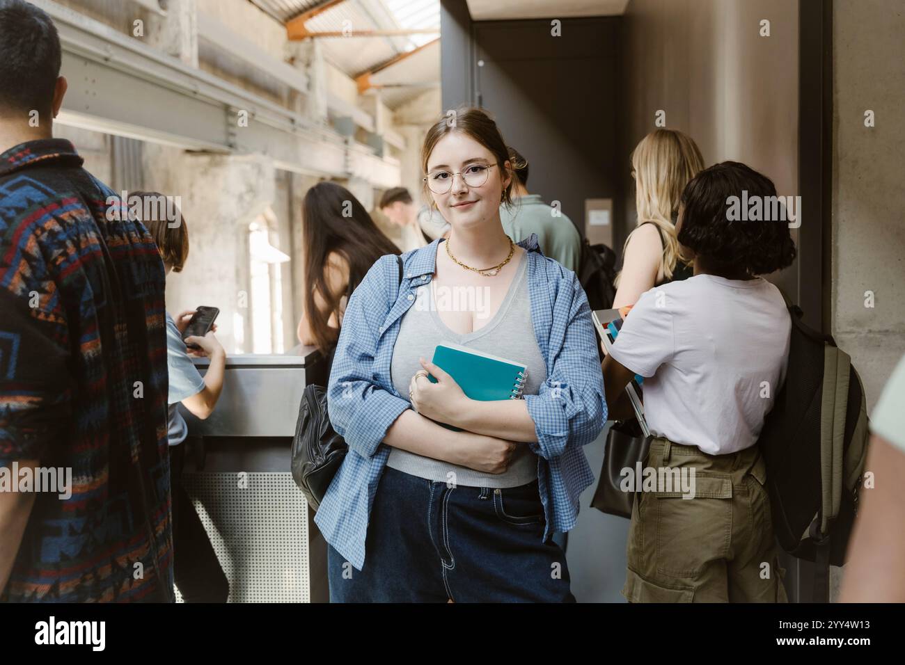 Ritratto di una giovane donna sorridente che tiene un libro mentre si trova vicino agli amici nel corridoio del college Foto Stock