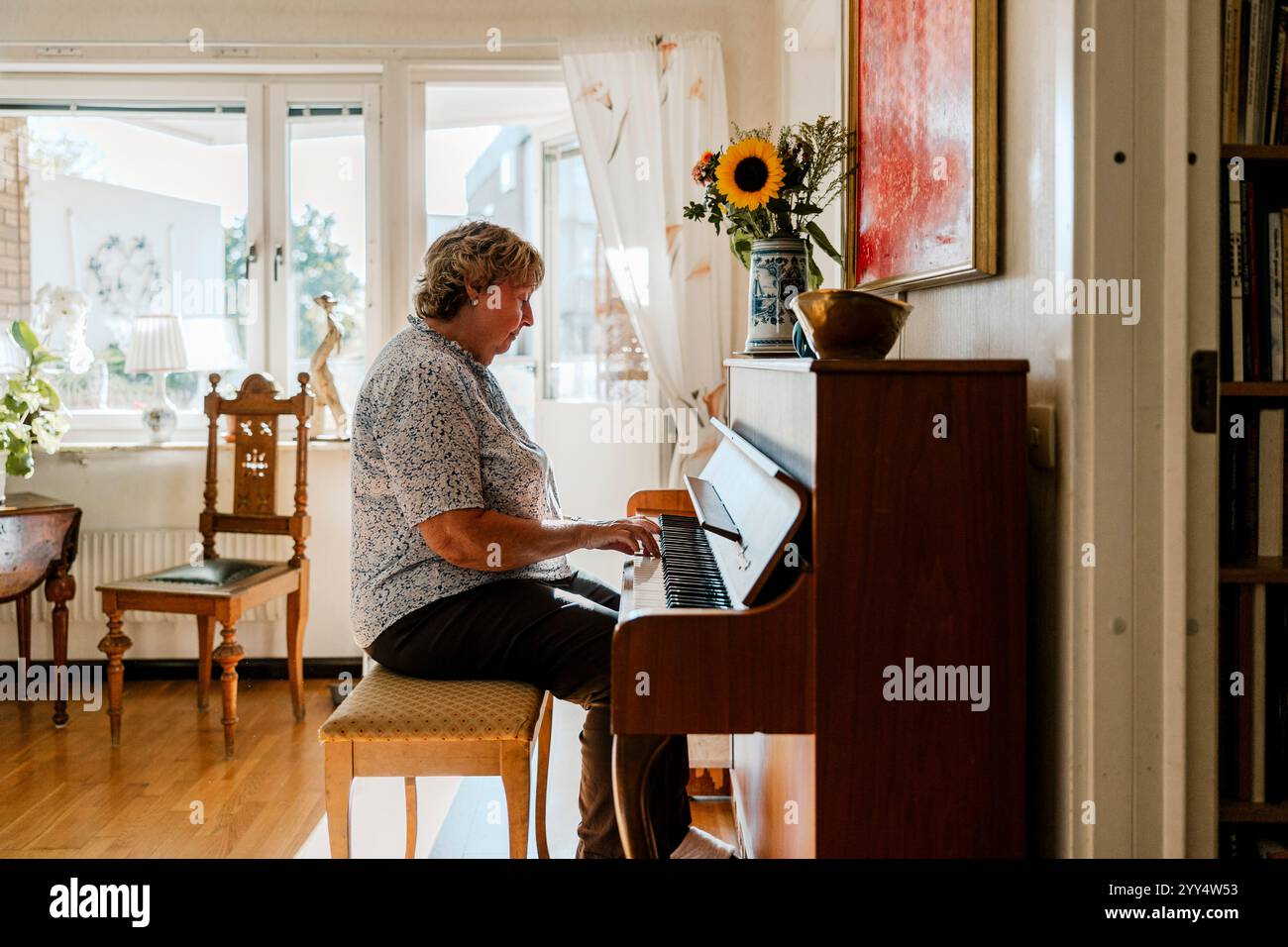 Vista laterale della donna anziana che suona il pianoforte nel soggiorno di casa Foto Stock