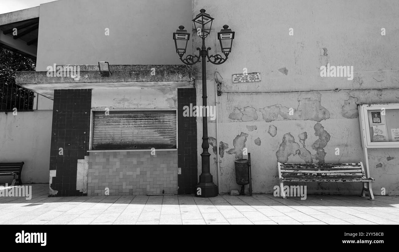 Telti, Italia, 7 aprile 2024. Uno scorcio bianco e nero di un lampione stradale e della vecchia edicola su un lato della piazza principale del paese durante una S. Foto Stock