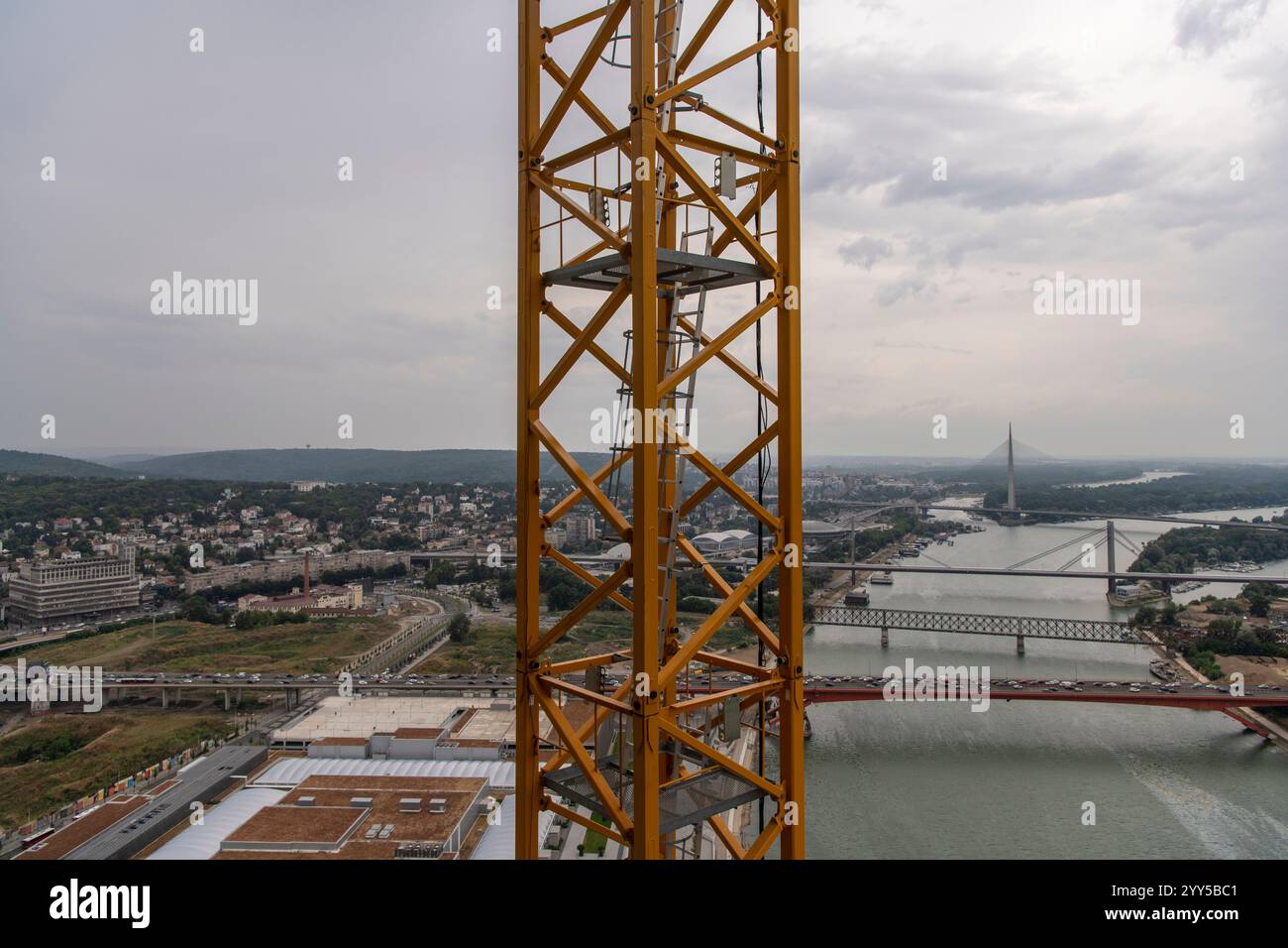 Vista ravvicinata della scala gialla di accesso alla gru, scala in acciaio. Cantiere di grattacielo a grattacielo. Splendido fiume panoramico, ponti e. Foto Stock