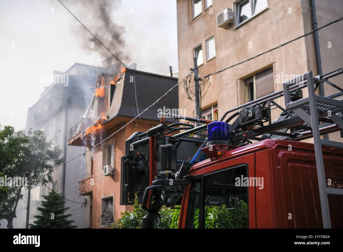 Immagine ravvicinata di luci blu e sirene su un camion dei vigili del fuoco, con un edificio in fiamme sullo sfondo. Foto Stock
