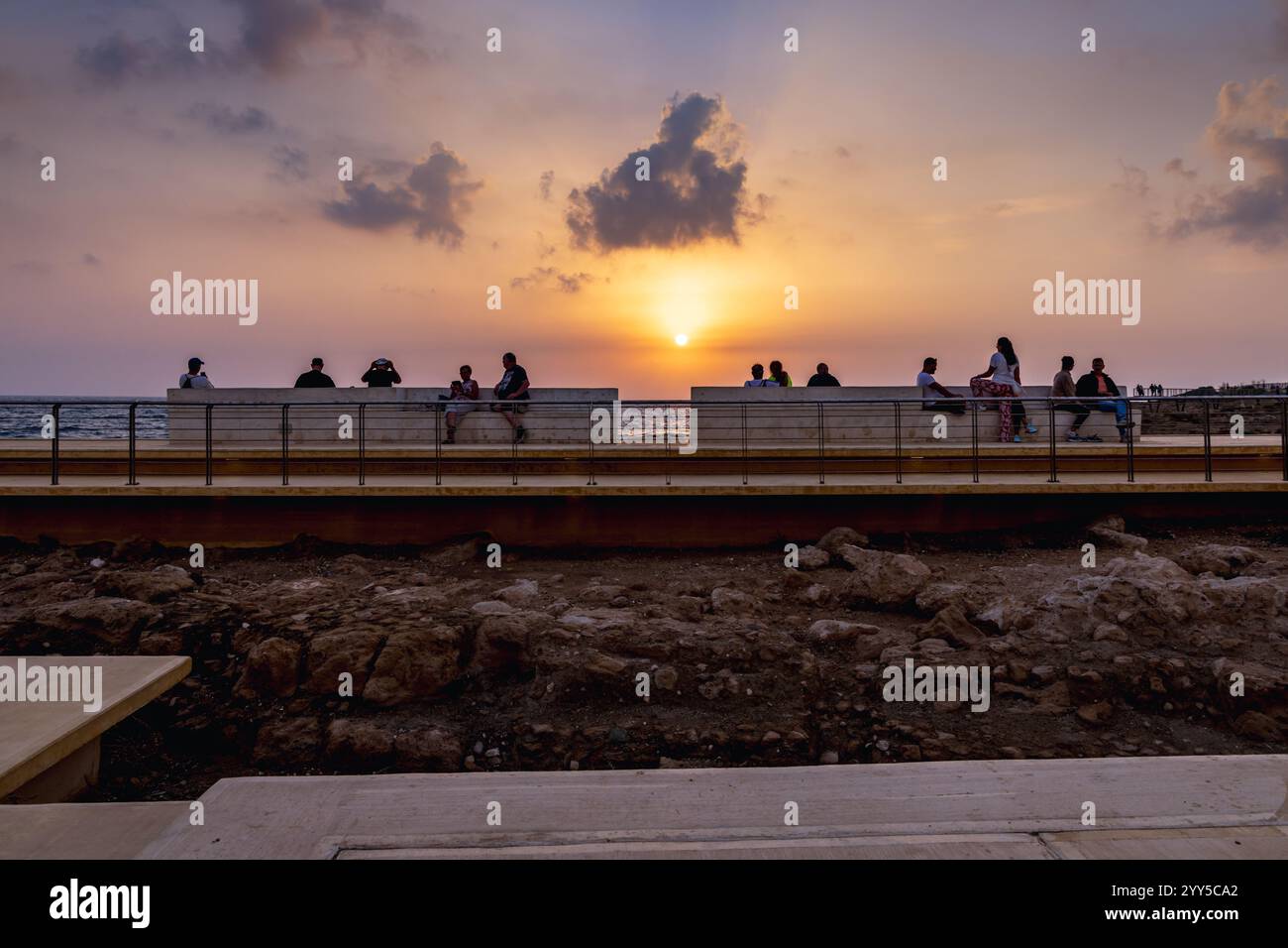 Persone che godono di una vista del tramonto dalla passerella costiera vicino al Castello di Paphos, Cipro Foto Stock