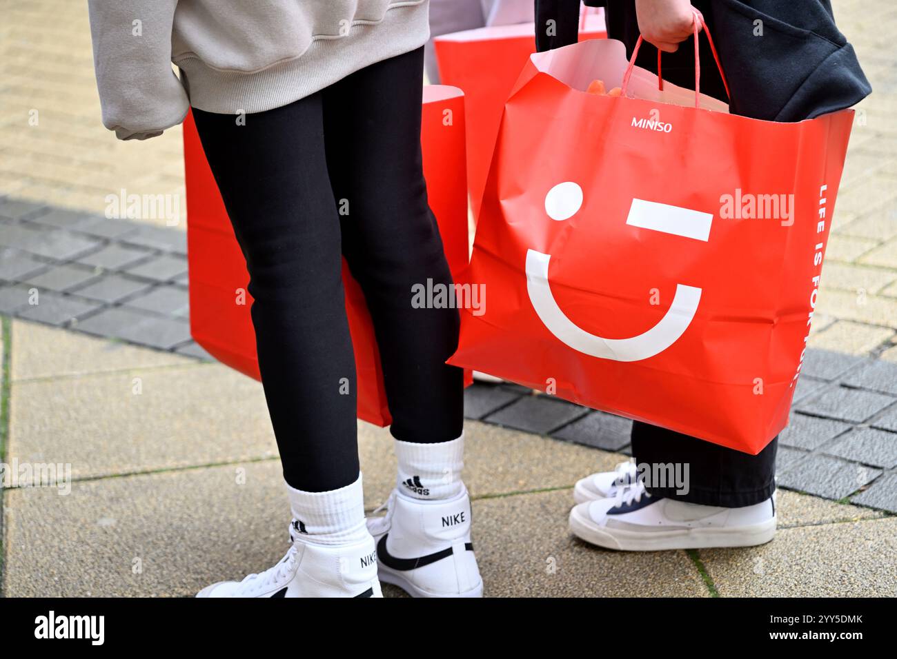 Due persone che trasportano borse per la spesa rosse dal negozio di moda Miniso fast fashion Foto Stock