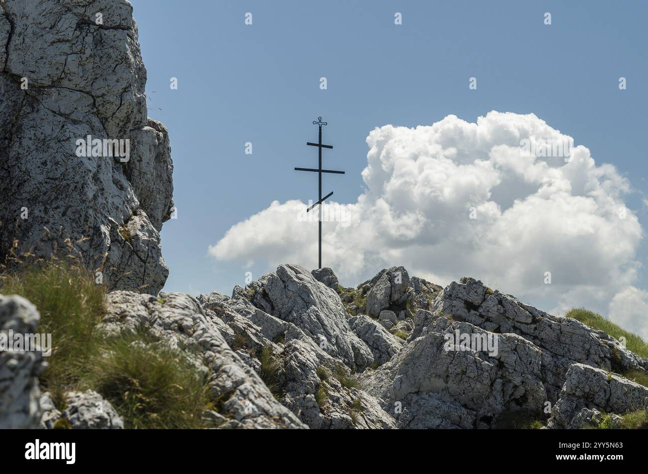Una croce di metallo su un terreno roccioso adagiato su uno sfondo di nuvole in un cielo blu, 16.12.2024 Foto Stock