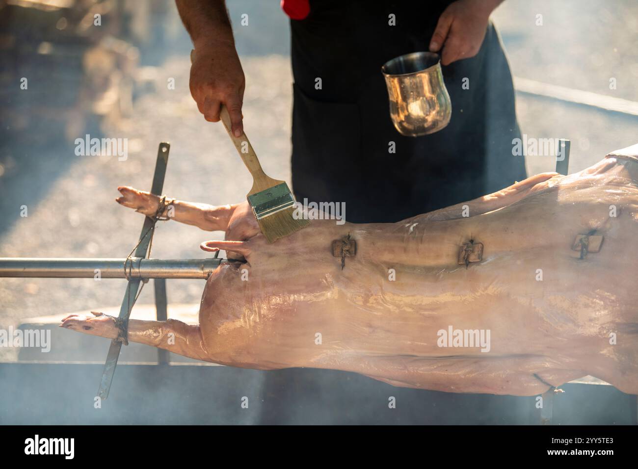 Un giovane maialino da latte su uno spiedino. Maiale tostato intero su un acciaio rotante sputare con fuoco e fumo. Griglia tradizionale della Serbia, nei Balcani, campagna Foto Stock