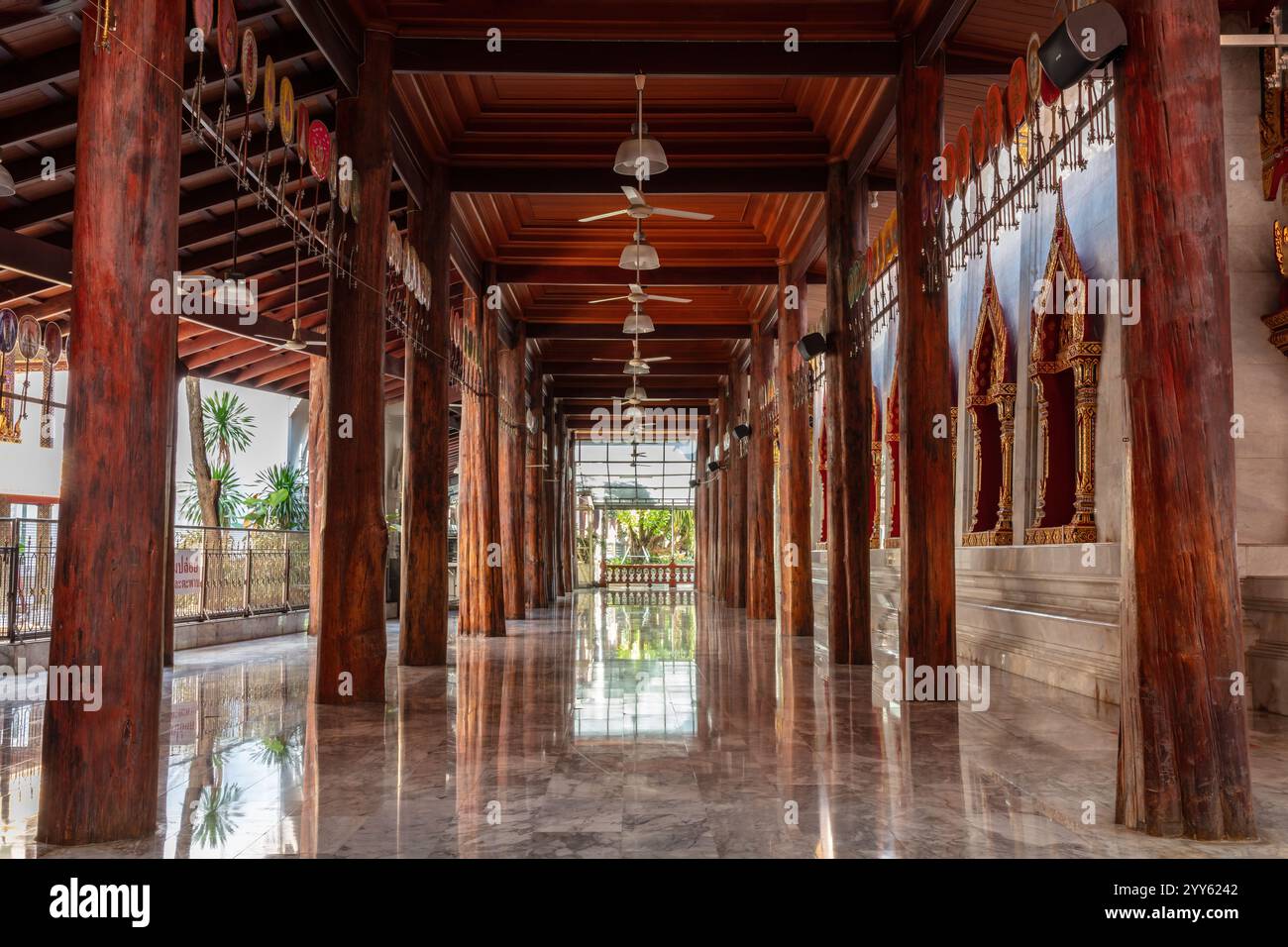 Corridoio esterno al Wat Paknam Phasi Charoen a Bangkok, Thailandia. Colonne e soffitto in legno; pavimento in marmo e pietra con riflessi. Foto Stock