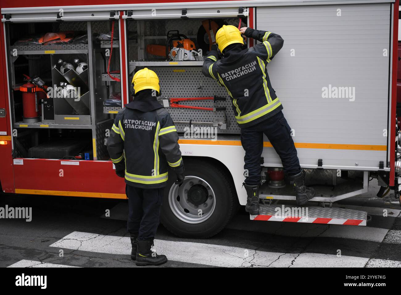 Due vigili del fuoco prendono in fretta le attrezzature necessarie dal camion dei vigili del fuoco prima di iniziare una missione di salvataggio a Belgrado, in Serbia. Foto Stock