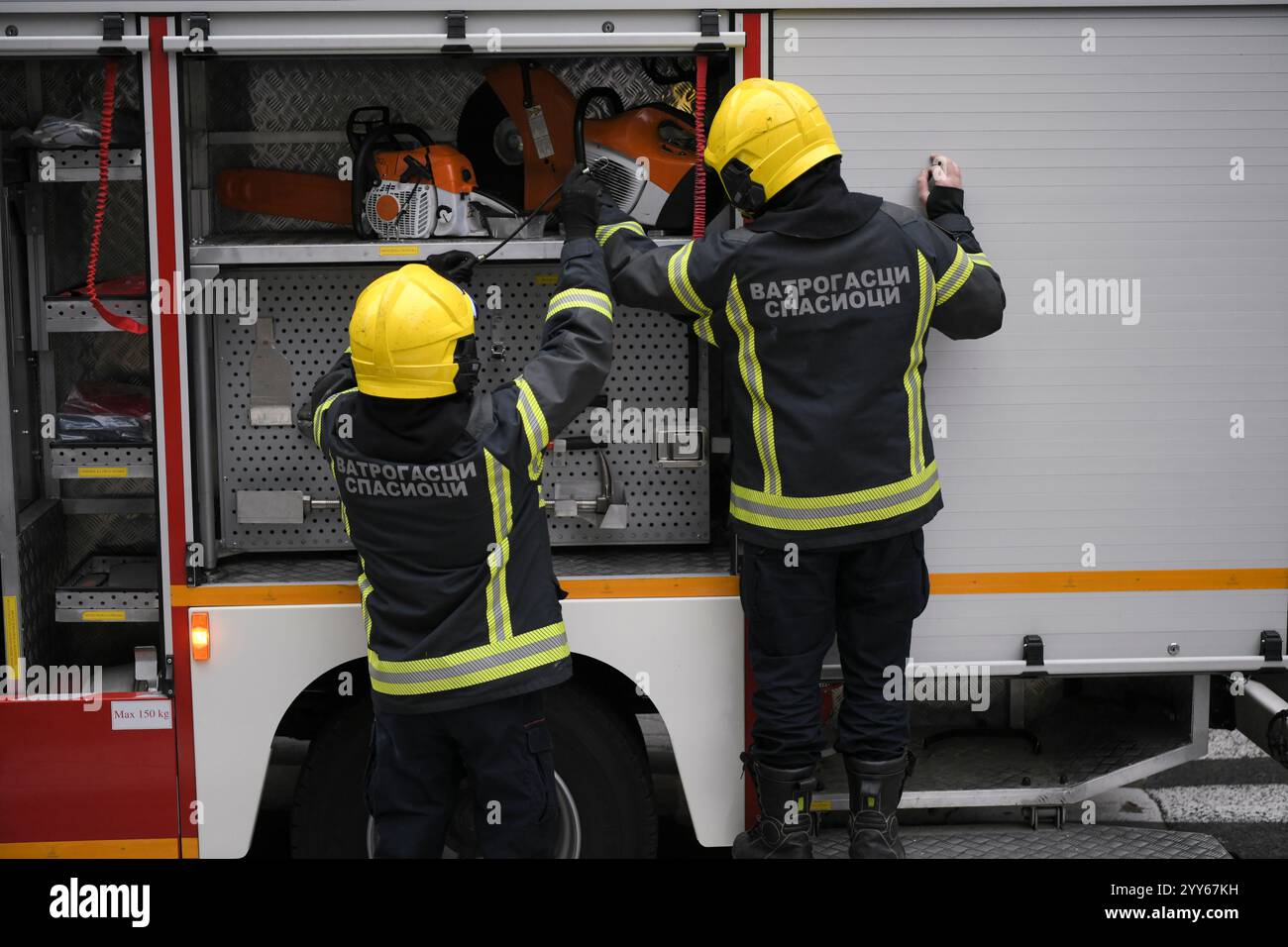 Due vigili del fuoco prendono in fretta le attrezzature necessarie dal camion dei vigili del fuoco prima di iniziare una missione di salvataggio a Belgrado, in Serbia. Foto Stock