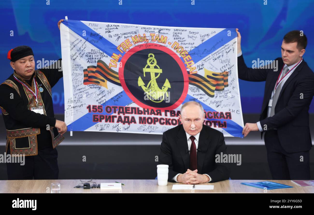 Mosca, Russia. 19 dicembre 2024. Il presidente russo Vladimir Putin, sorride mentre gli uomini tengono dietro di lui una replica della 155a Brigata Marines dello striscione della flotta del Pacifico durante la conferenza stampa annuale e la call-in show al Gostinny Dvor, 19 dicembre 2024 a Mosca, Russia. La 155th Marine Brigade sta prestando servizio in prima linea lungo la regione di Kursk nella guerra russo-Ucraina. Crediti: Gavriil Grigorov/piscina del Cremlino/Alamy Live News Foto Stock