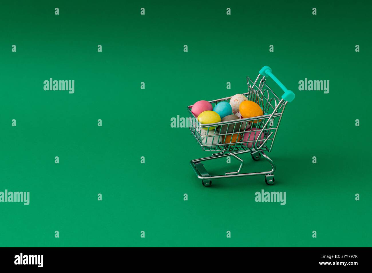 Composizione pasquale realizzata con uova di Pasqua colorate nel carrello della spesa su sfondo verde. Concetto di Pasqua minimalista. Layout creativo per le festività. Foto Stock