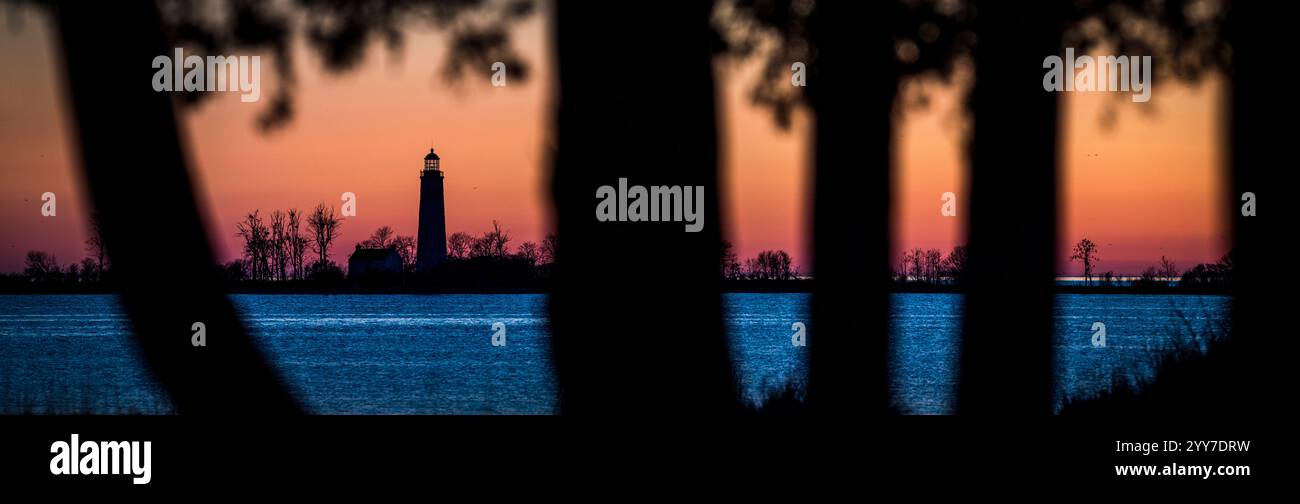 Faro di Chantry Island incorniciato da alberi sagomati al tramonto, con vibranti tonalità di arancione e blu che si riflettono sull'acqua, Southampton, IN Canada Foto Stock