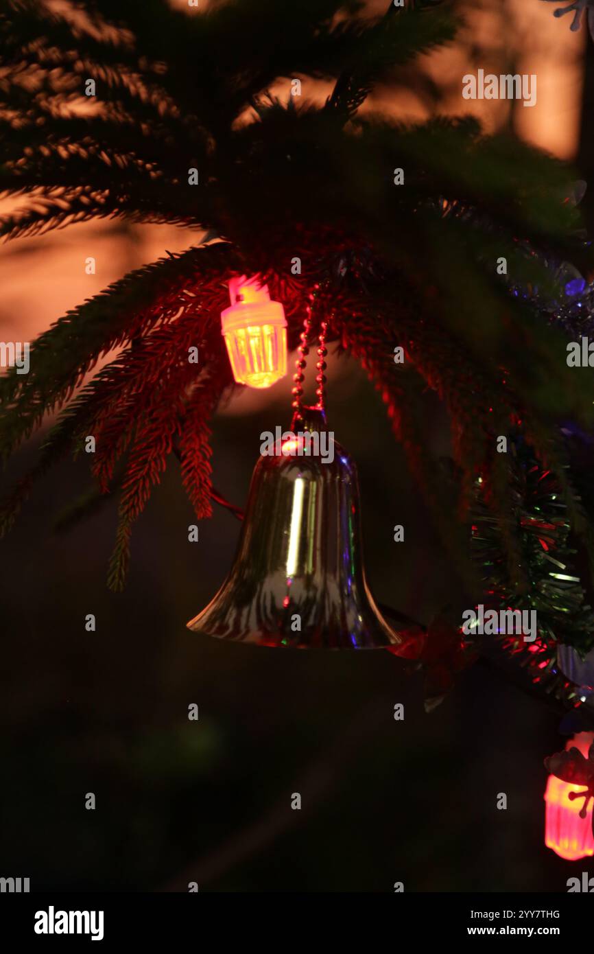 Festeggiamenti natalizi e di Capodanno, campana dorata appesa al ramo di pino, decorazione di ornamenti a campana Jingle garland primo piano su sfocatura Foto Stock