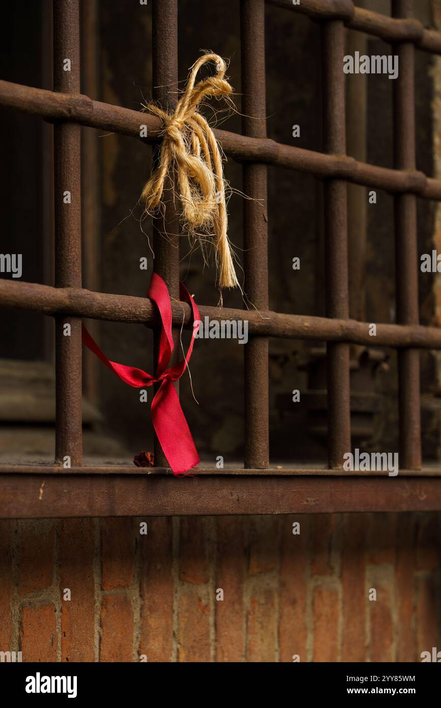 Un nastro rosso e un pezzo di corda legato a barre arrugginite Foto Stock