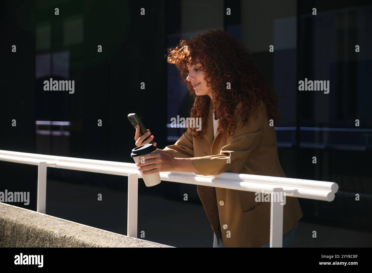 Donna d'affari che si gode una pausa caffè, usa il telefono e sorride Foto Stock
