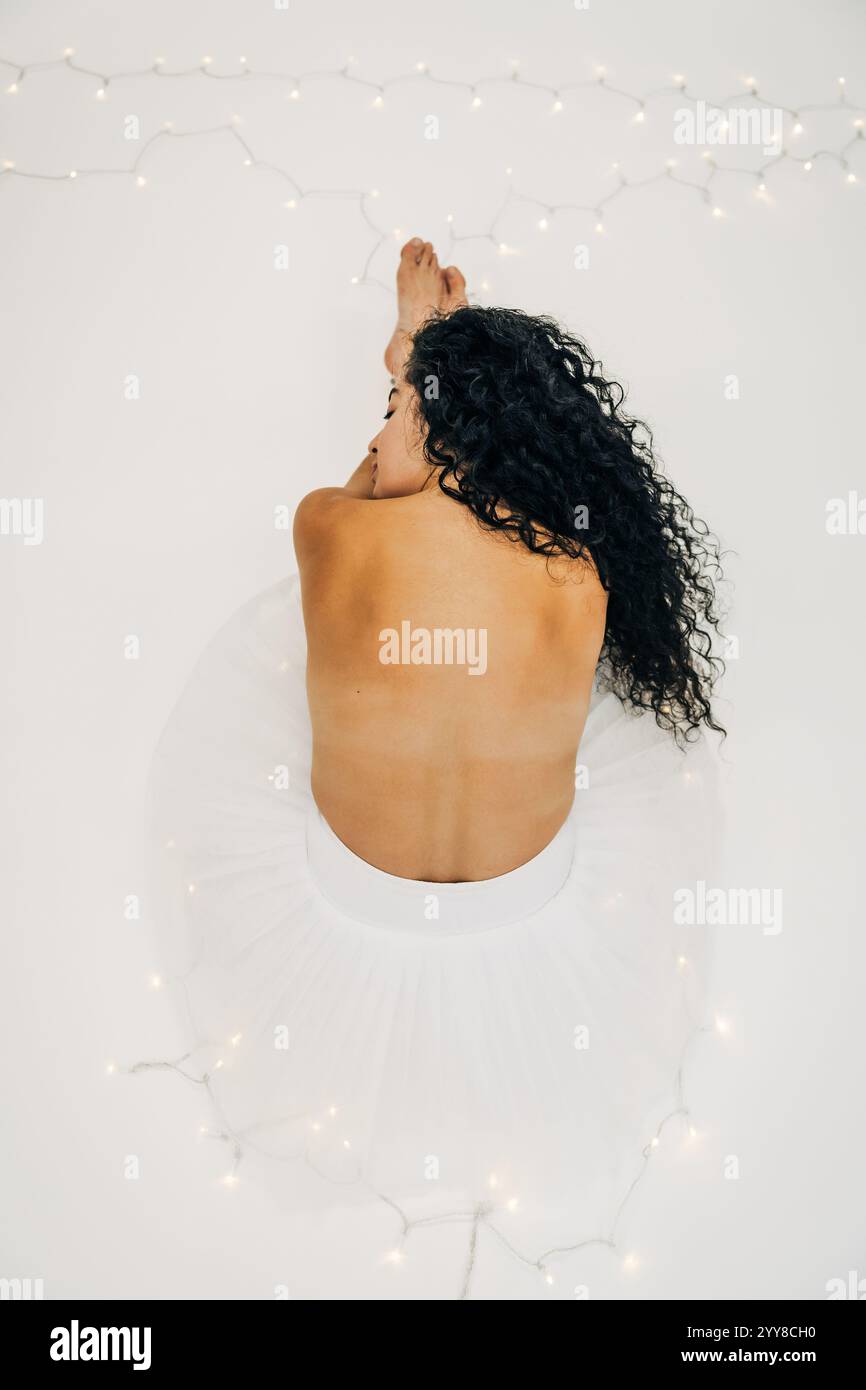 Ballerina in tutù bianco con capelli ricci si adagia su uno sfondo bianco Foto Stock