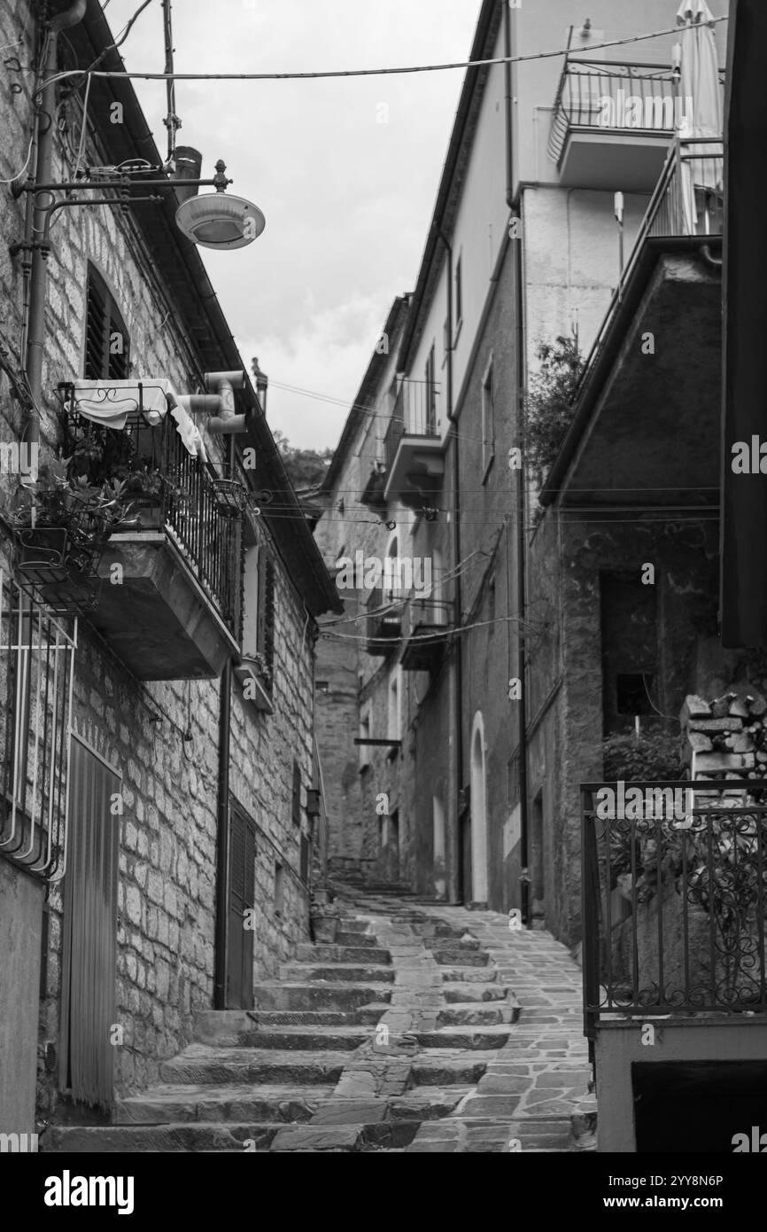 Ripida strada in pietra in uno storico villaggio europeo, fiancheggiata da tradizionali edifici in pietra con balconi e vegetazione. Atmosfera intramontabile e pittoresca Foto Stock