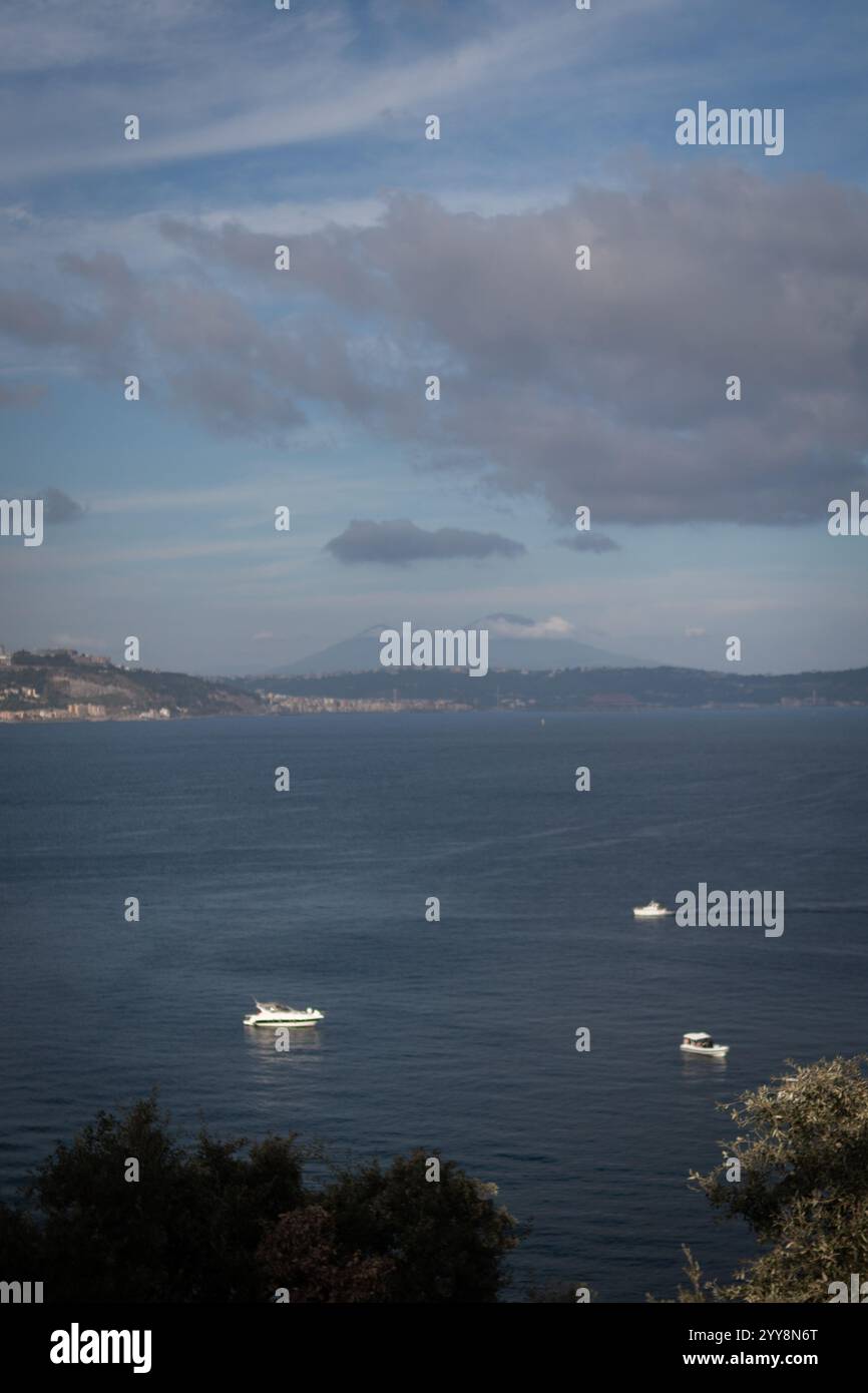 Vista panoramica del mare con piccole barche e montagne lontane sotto un cielo parzialmente nuvoloso. Tranquillo e naturale paesaggio costiero di Napoli. Foto Stock