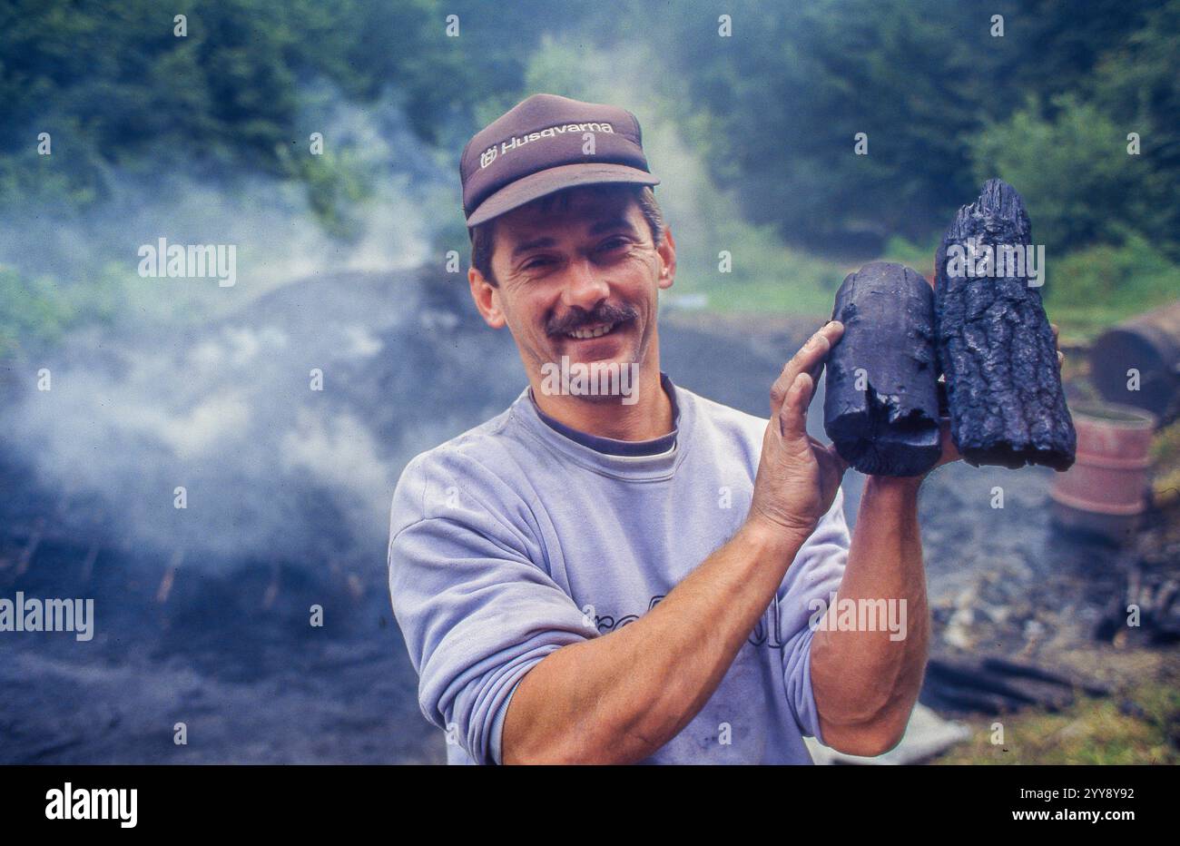 Ungheria, il lavoratore forestale mostra carbone fresco proveniente da un tumulo di carbone con un nuovo mucchio dietro di lui. Foto Stock