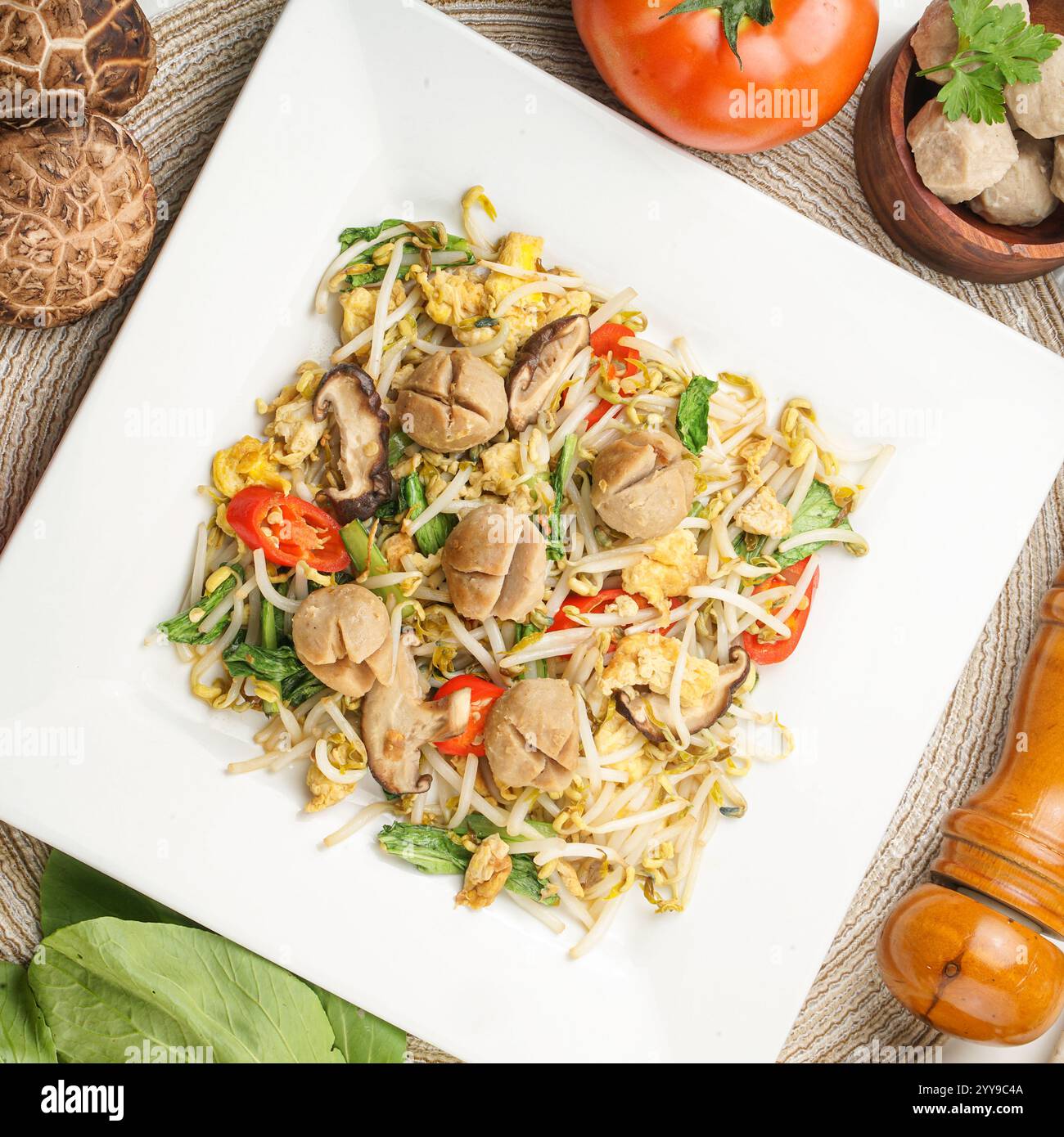 Un delizioso piatto fritto in padella con polpette di manzo, germogli di soia, funghi, uova e verdure fresche, servito su un piatto quadrato, un autentico pasto asiatico Foto Stock