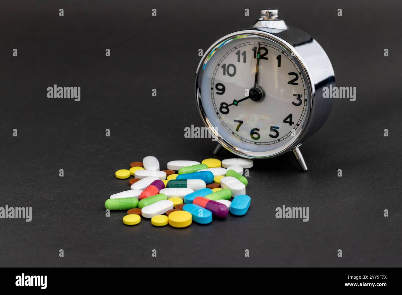 Pillole medicinali con sveglia su sfondo nero Foto Stock