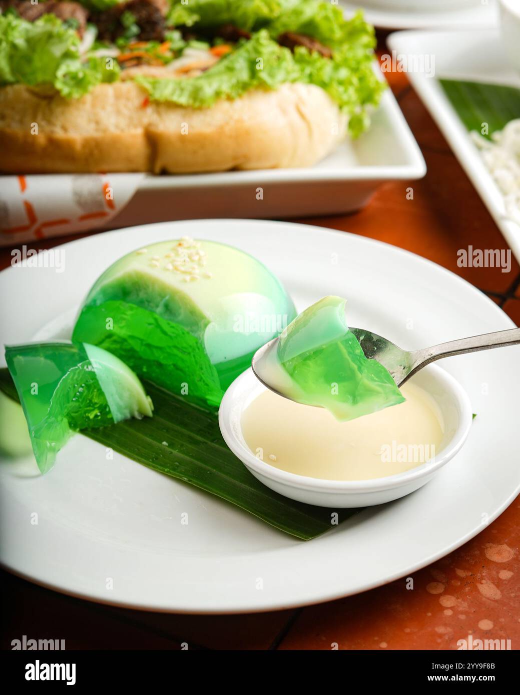 Un delicato e colorato dessert vietnamita in gelatina di panda servito su una foglia di banana con un lato di crema di cocco, splendidamente placcato Foto Stock