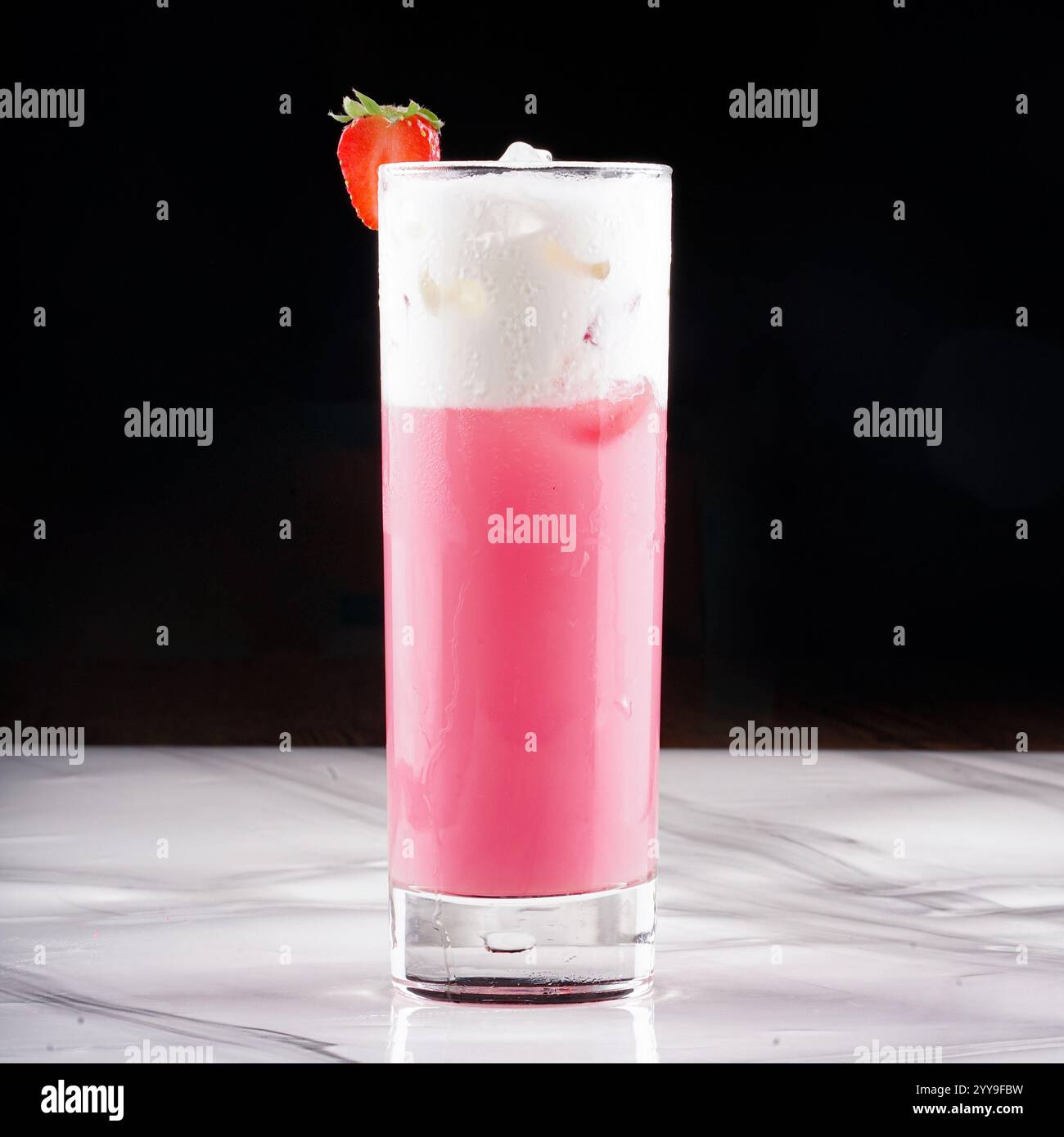 Deliziosa bevanda ghiacciata di fragole e panna servita in un bicchiere trasparente, ricoperta di panna montata, fette di fragole fresche e foglie di menta, circondata Foto Stock