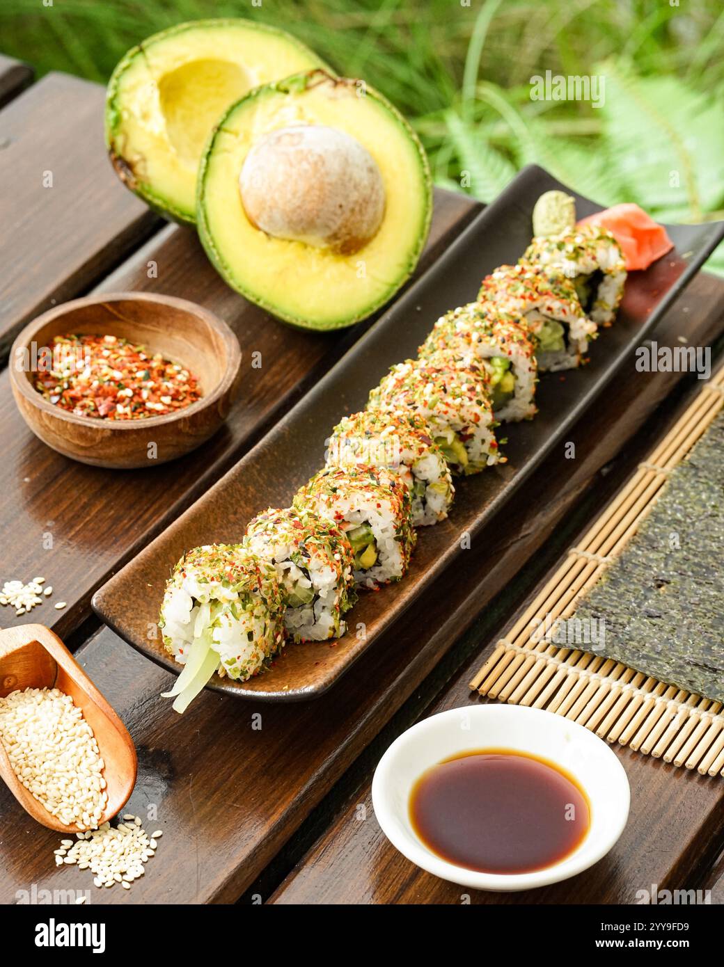 Un piatto di sushi ben organizzato con ripieni di avocado e frutti di mare, servito con salsa di soia, wasabi e zenzero sottaceto su un tappeto di bambù Foto Stock