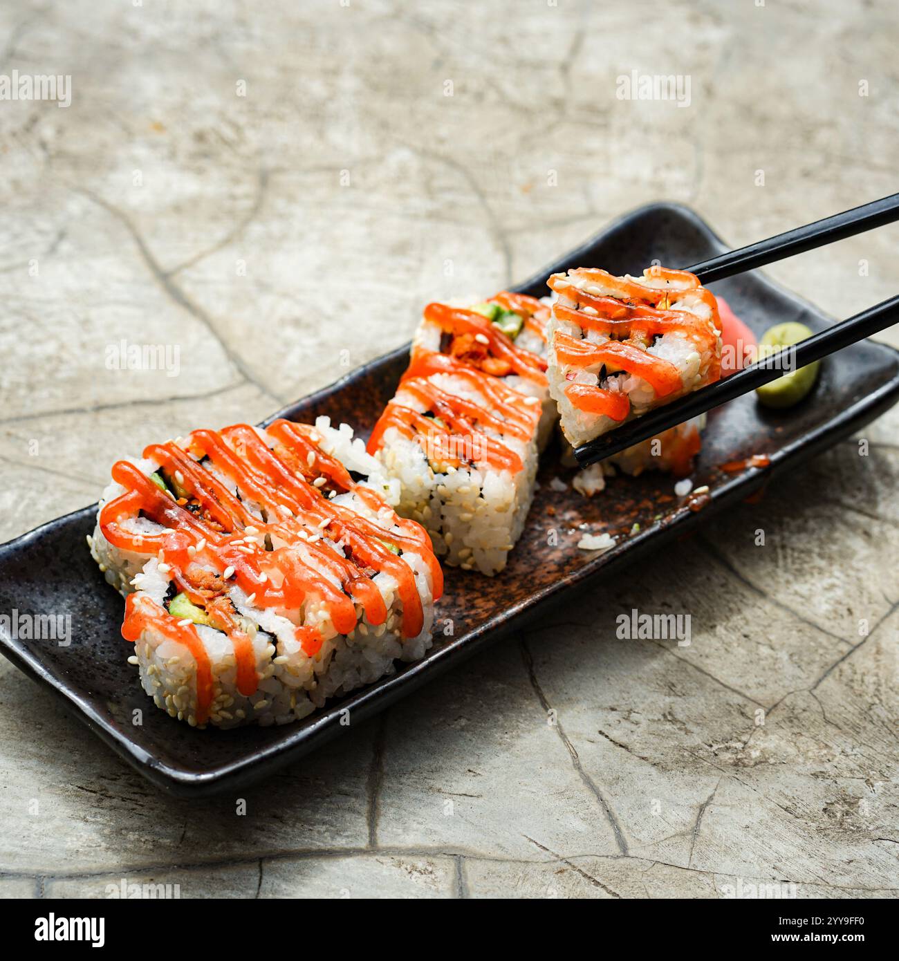 Un piatto di sushi ben organizzato con ripieni di avocado e frutti di mare, servito con salsa di soia, wasabi e zenzero sottaceto su un tappeto di bambù Foto Stock