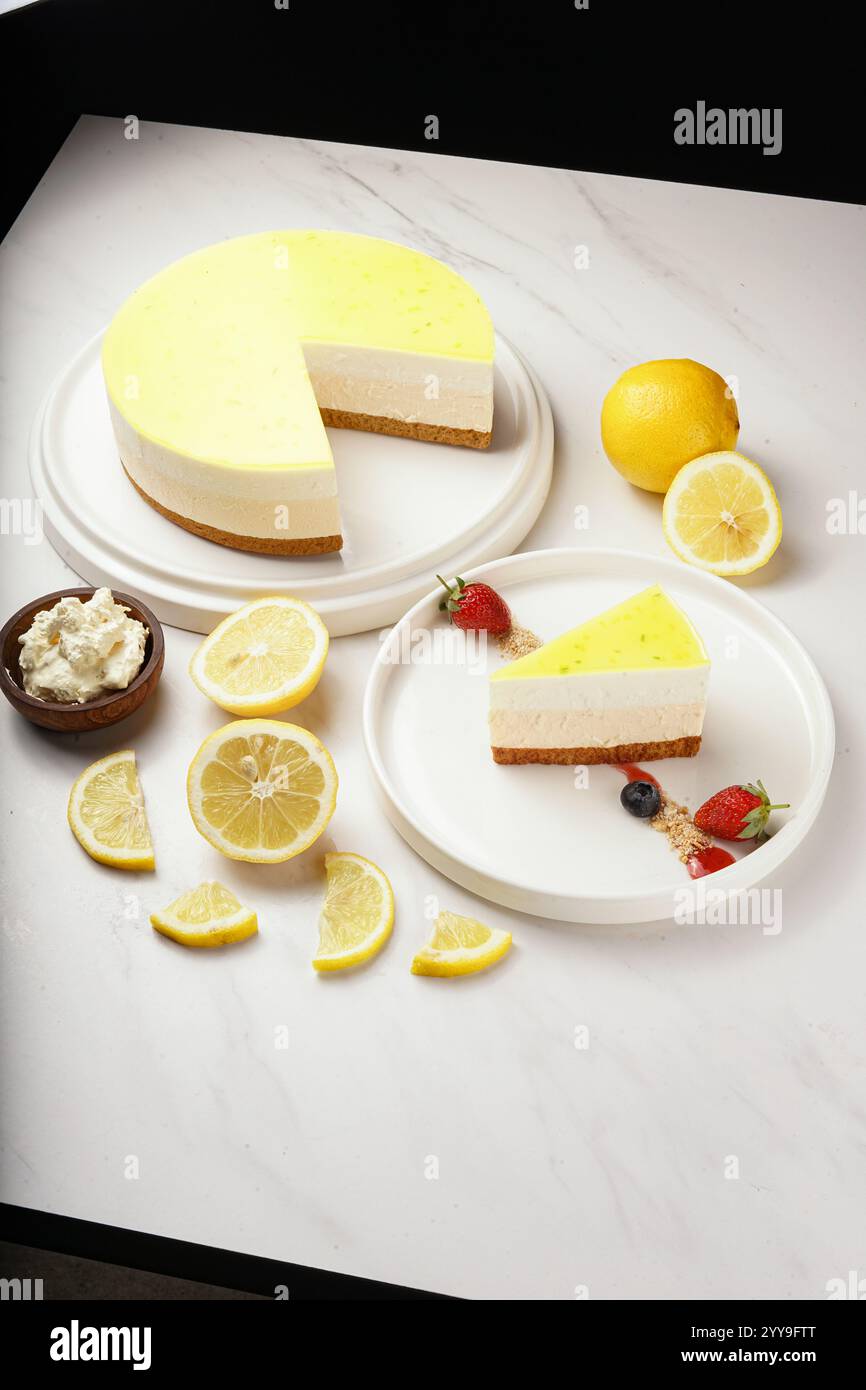 Rinfrescante cheesecake al limone con crosta di biscotti, condita con una sfarzosa glassa al limone. Una fetta viene servita con fragole fresche e mirtilli Foto Stock