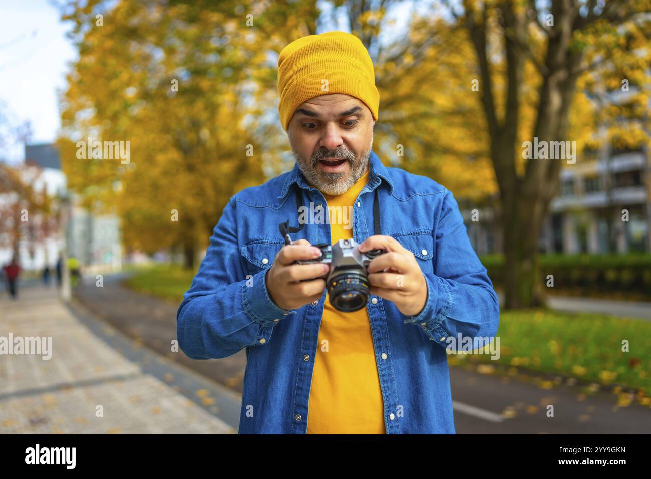 Un turista maturo che guarda le foto sullo schermo di una fotocamera mentre fotografa la città in autunno Foto Stock