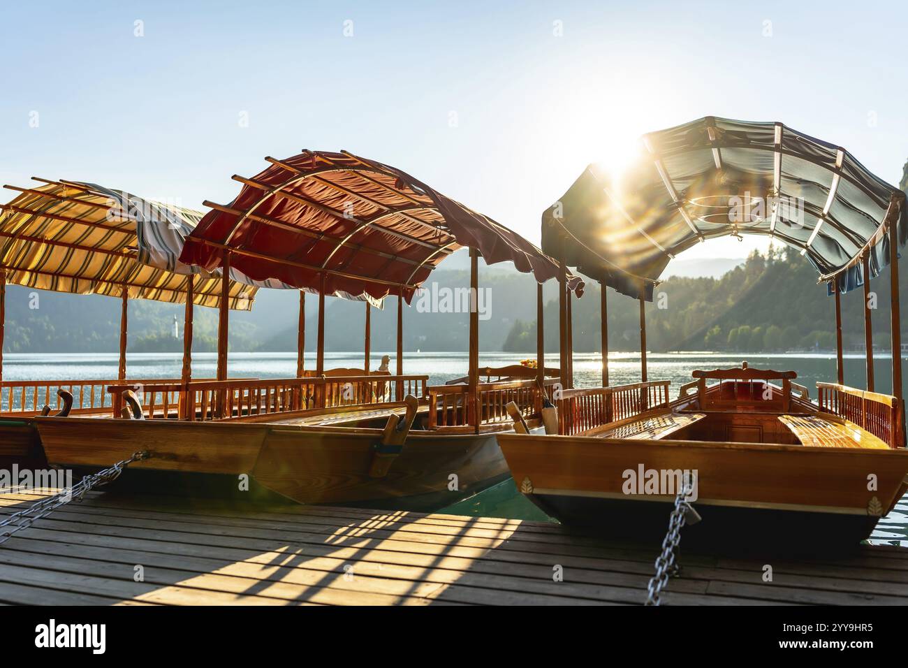 Barche turistiche in legno, note come pletnas, ormeggiate presso un molo sul lago dissanguato in slovenia, bagnate dalla luce dorata dell'alba Foto Stock