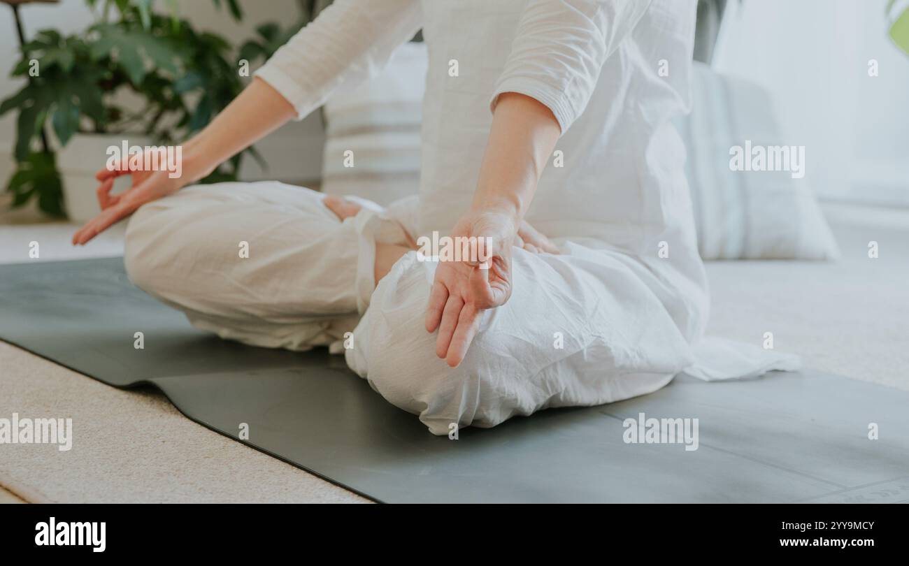 Una donna che indossa abiti bianchi seduti in loto con mudra Gyan, che fa yoga a casa, meditazione, yoga a casa Foto Stock